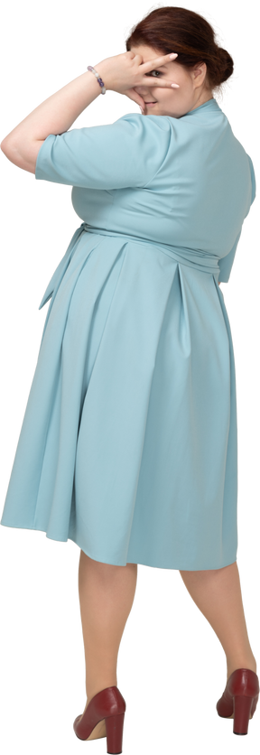 V記号を示す青いドレスを着た女性の背面図