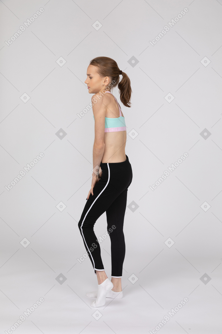 Side view of a shy teen girl in sportswear holding hands together