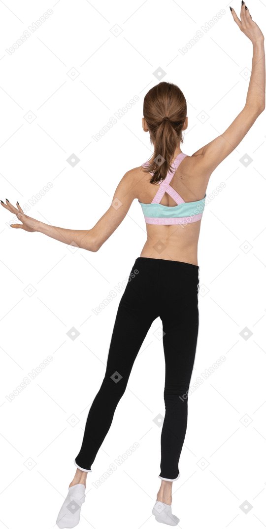 Vista traseira de uma adolescente em roupas esportivas levantando as mãos e colocando a perna de lado