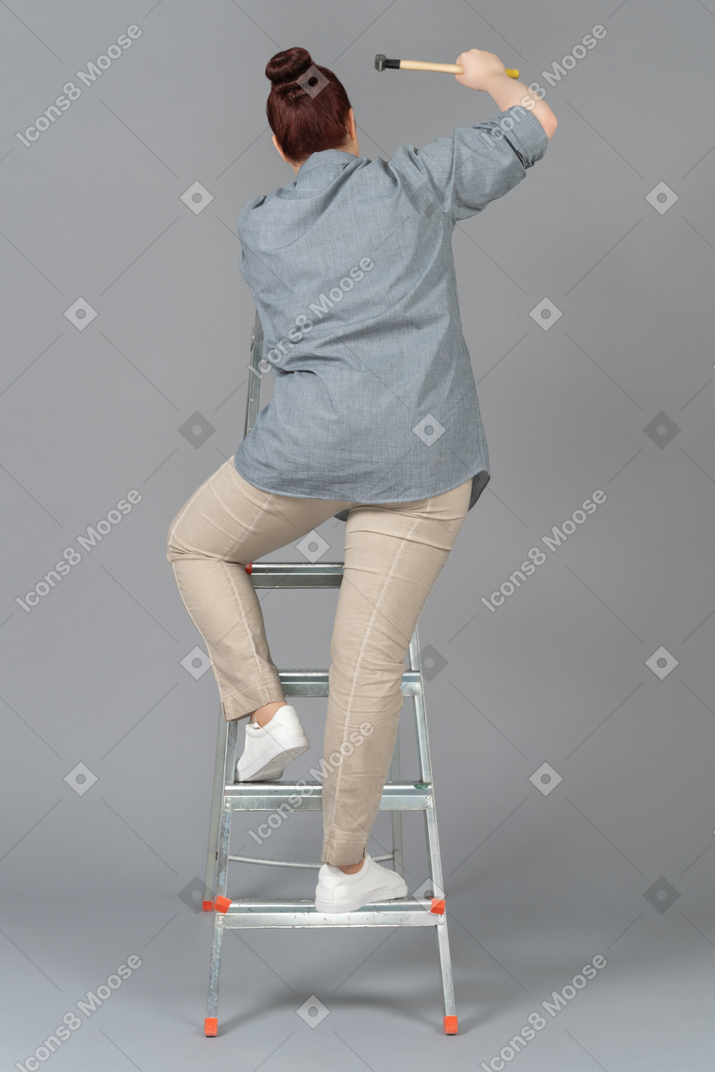 Young woman standing on stepladder backwards and hammering