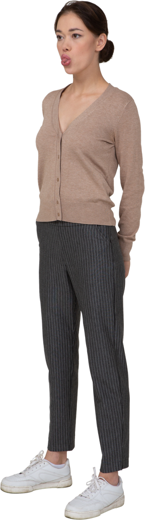 Vista de tres cuartos de una joven en suéter y pantalones mostrando la lengua