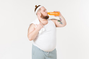一个穿运动服的胖子从瓶子里喝一杯软饮料
