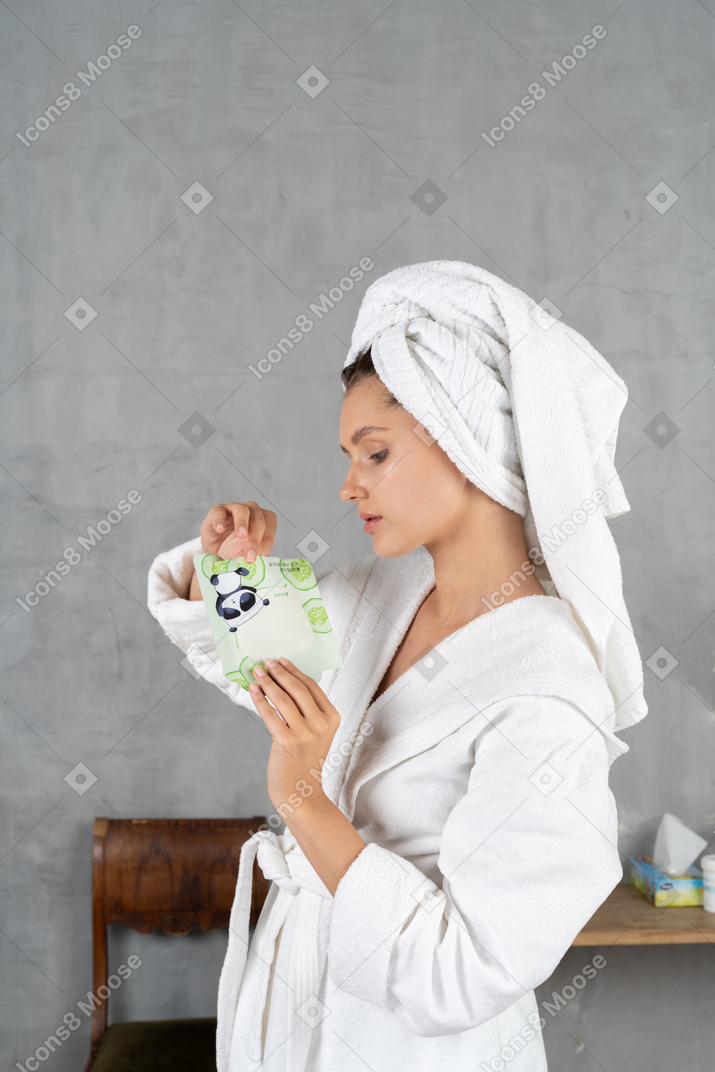 Woman in bathrobe tearing open a sheet mask pack