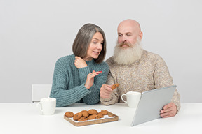 Couple âgé assis à la table et regarder un film sur tablette