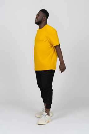 Vista di tre quarti di un giovane uomo dalla pelle scura con una maglietta gialla che si tiene per mano dietro