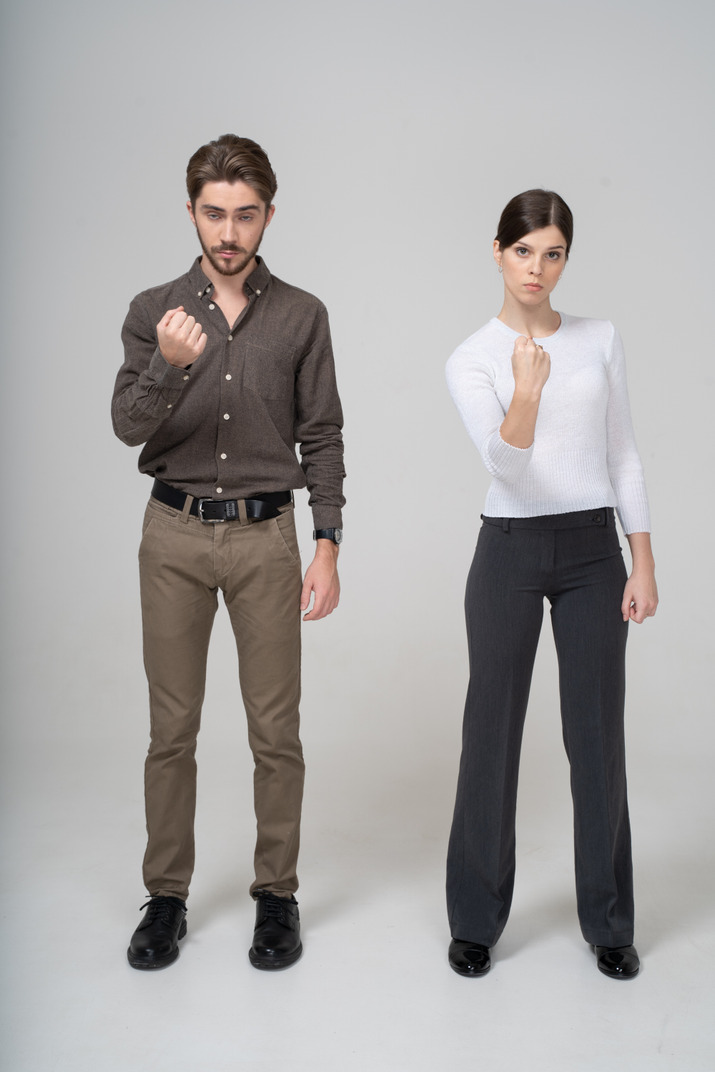 Front view of a strict young couple in office clothing showing fist