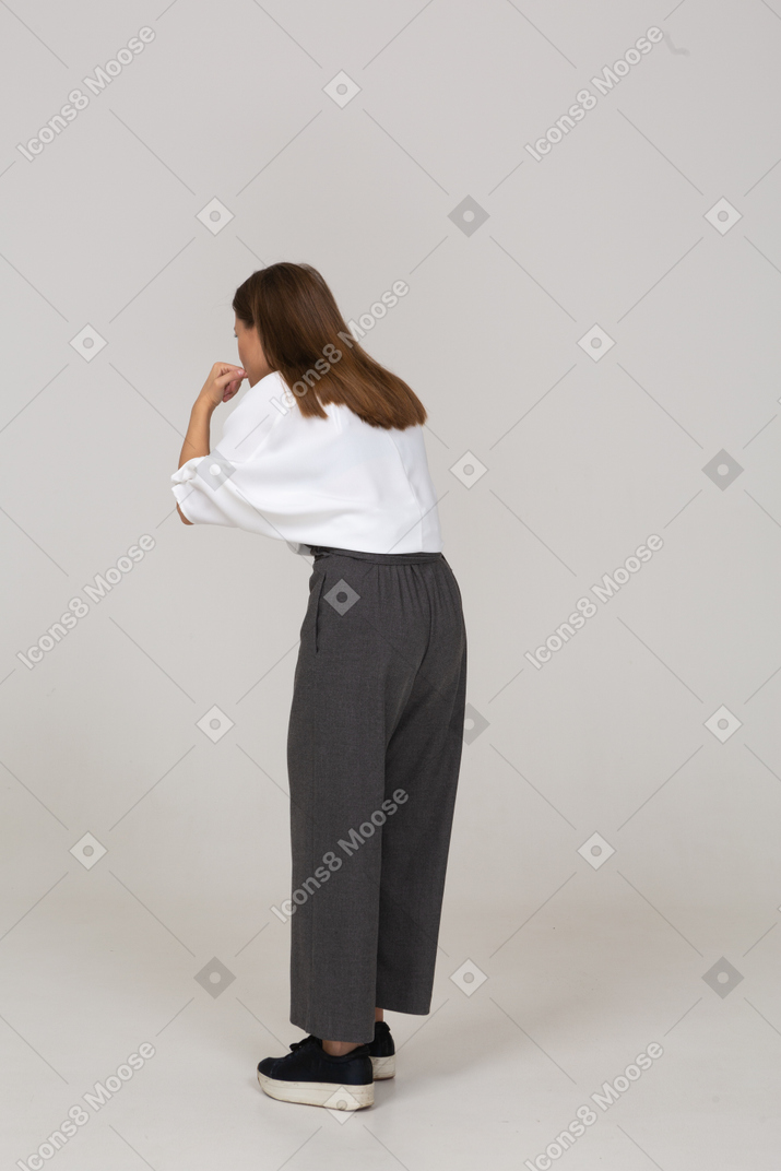 Three-quarter back view of a whistling young lady in office clothing leaning forward