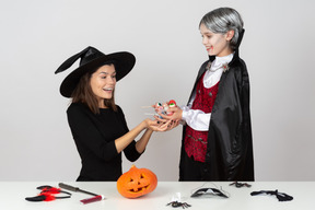 Ragazzo in costume da vampiro che mostra caramelle a sua mamma in costume da gatto