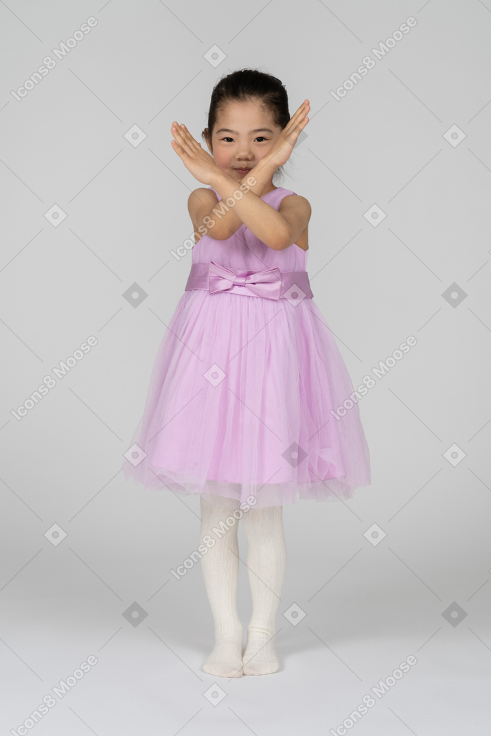 Retrato de una niña linda que hace la señal de stop con los brazos cruzados