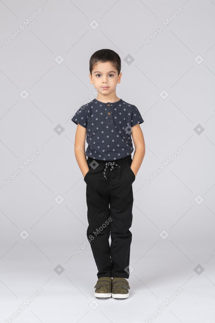 Front view of a cute boy posing with hands in pockets and looking at camera