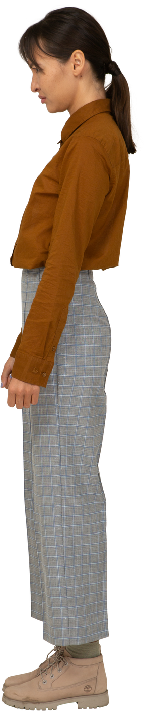 Vista lateral de uma jovem asiática descontente de calça e blusa, parada