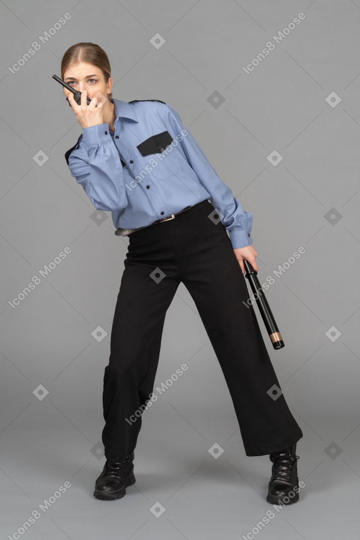 Female security guard bent to side speaking on the radio with a baton in hand