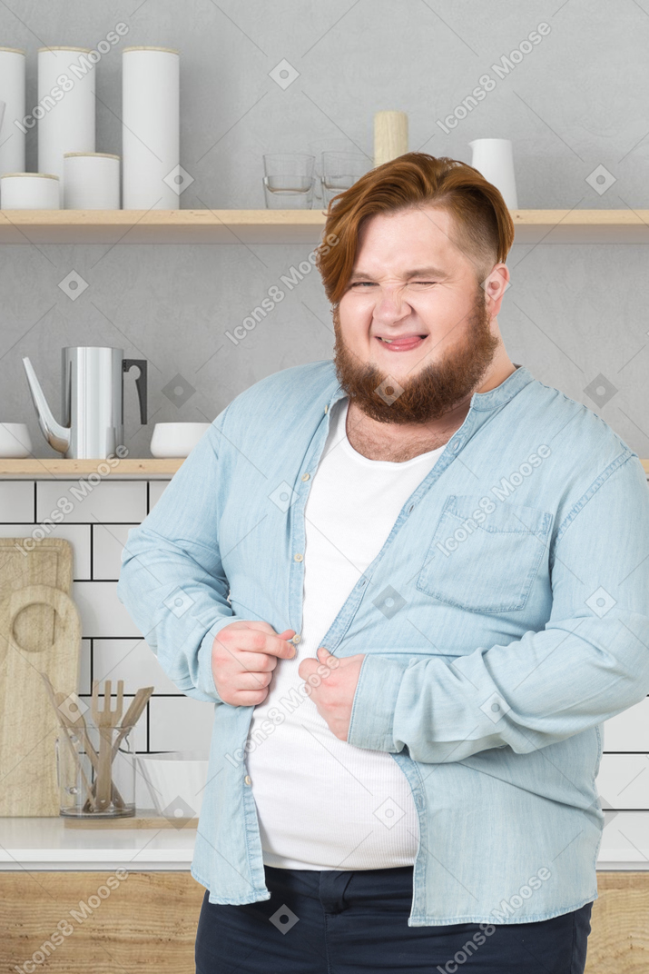 Uomo in una cucina che cerca di abbottonarsi la camicia