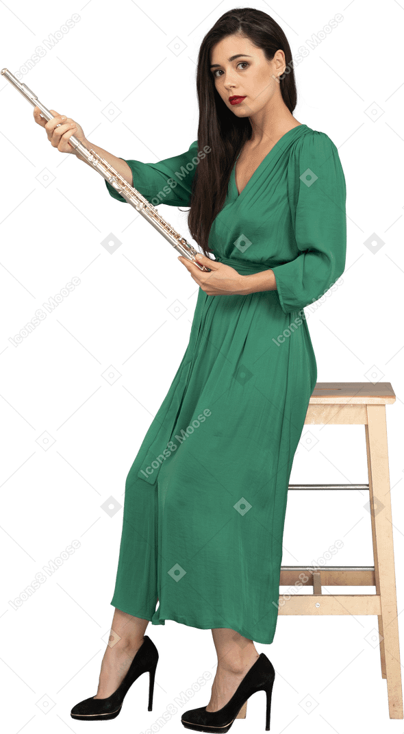 Vista lateral de uma jovem de vestido verde sentada em uma cadeira segurando um clarinete
