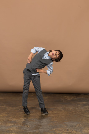 Vista frontal de un niño con traje gris de pie con las manos en las caderas