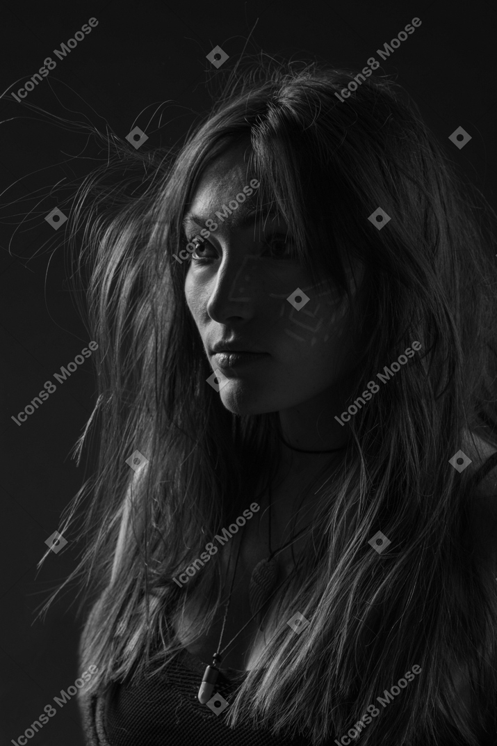 Noir ritratto di tre quarti di una giovane donna con arte facciale etnica e capelli disordinati