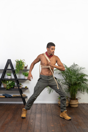 Determined young man standing with feet wide apart and holding a coil of rope