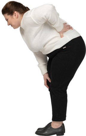 Женщина больших размеров в белом свитере страдает от боли в пояснице