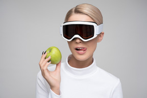 Young woman in ski goggles holding a green apple