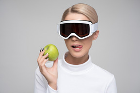 Mujer joven con gafas de esquí sosteniendo una manzana verde