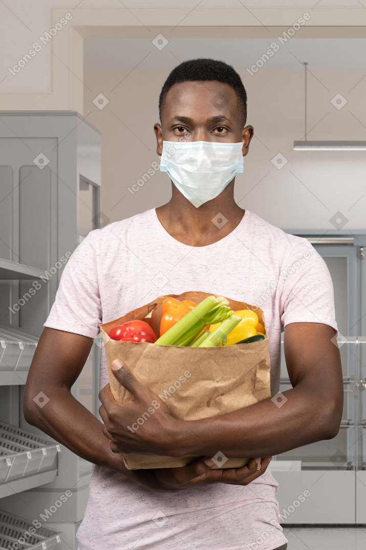 食料品の袋を保持しているフェイスマスクの男