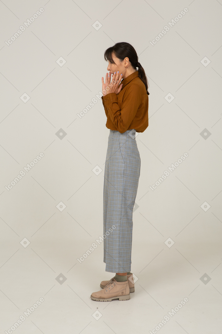 Side view of a shocked young asian female in breeches and blouse raising hands