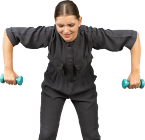Vue de face d'une jeune femme en combinaison faisant des exercices avec des haltères