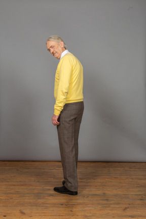 カメラを見て黄色のプルオーバーを着て不機嫌な老人の背面図