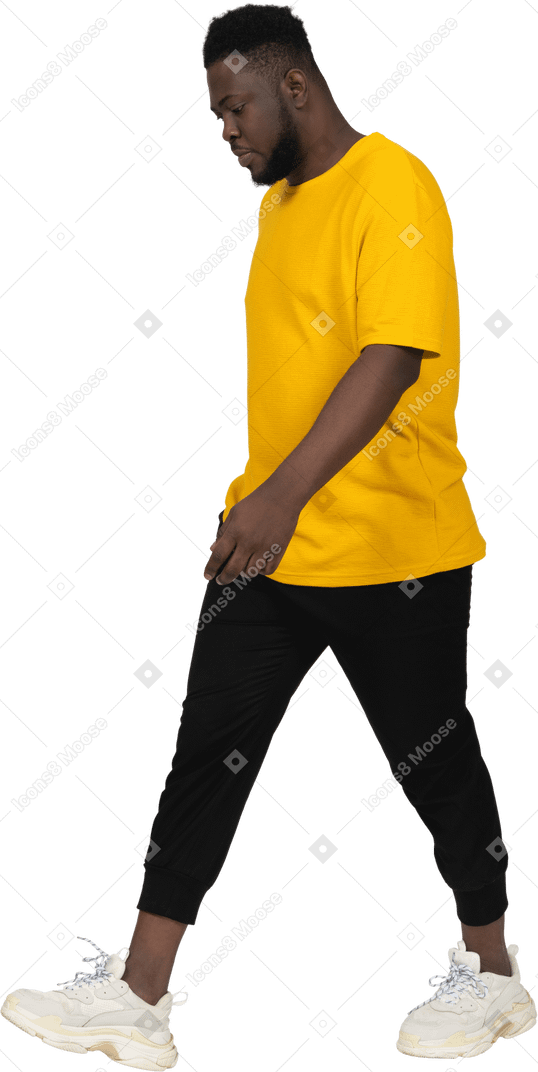 Three-quarter view of a walking young dark-skinned man in yellow t-shirt