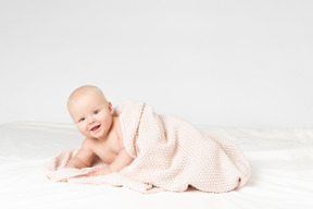 Smiling baby boy covered in beige knitted blanket