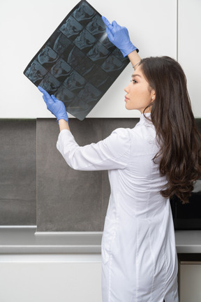 Vista traseira de uma jovem médica segurando uma imagem de raio-x e olhando para o lado