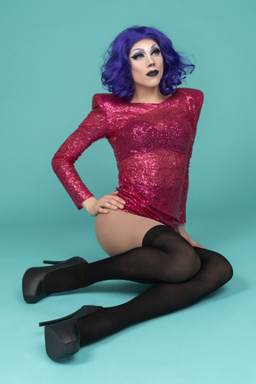 Portrait of a drag queen in pink dress sitting on the floor with knees bent