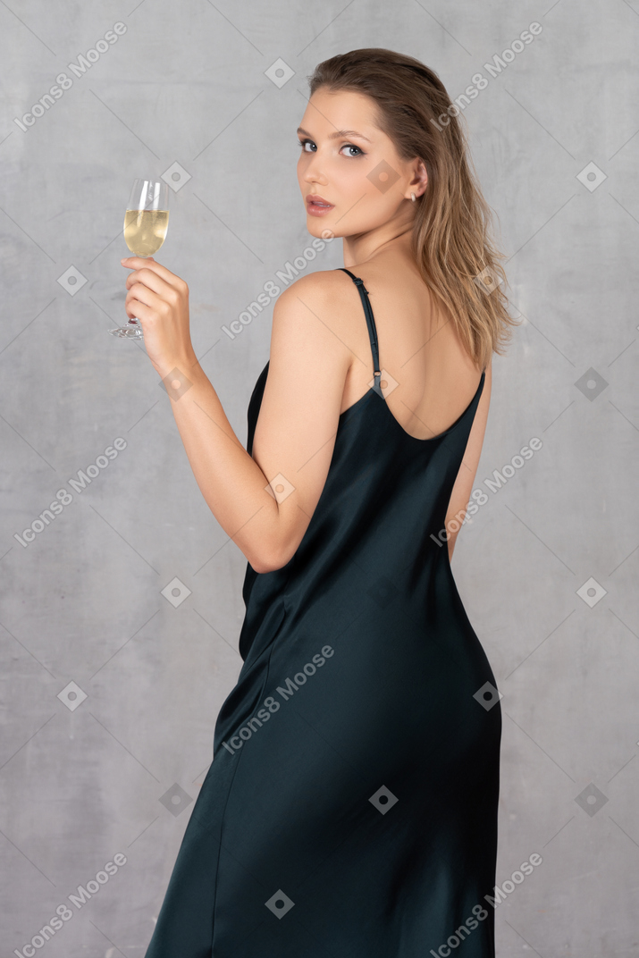 Vista traseira de uma jovem com vestido de noite segurando uma taça de champanhe
