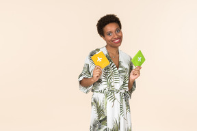 Black short-haired woman in a white and green dress, standing with two passports in her hands