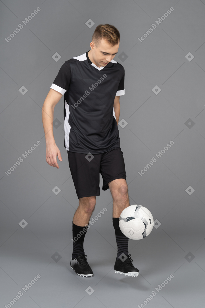 Vista de três quartos de um jogador de futebol masculino chutando uma bola