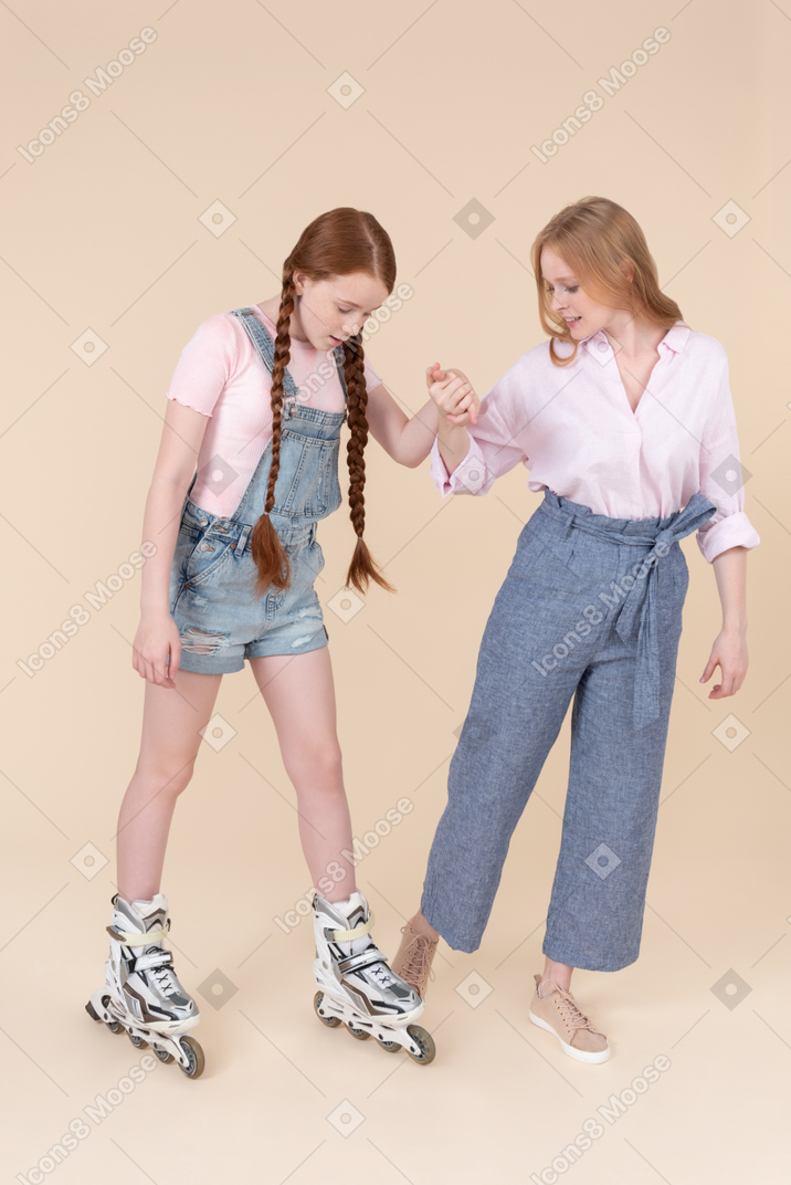 Young woman helping teen girl to stand on rollerblades