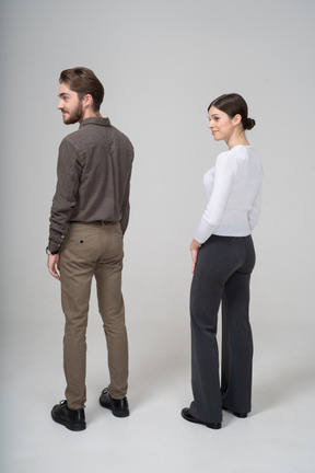 Vista posterior de tres cuartos de una joven pareja complacida en ropa de oficina