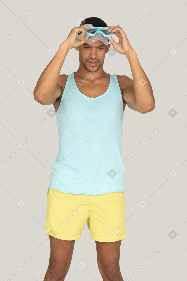 Man in blue tank top and yellow shorts puttting on swimming mask