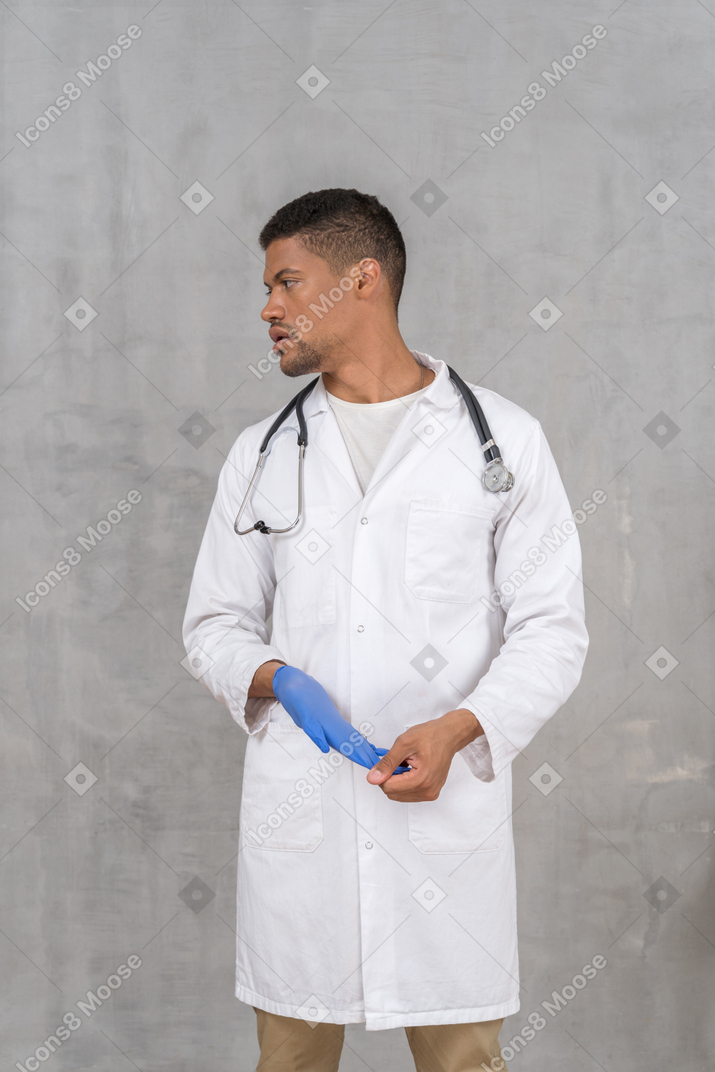 Молодой врач-мужчина снимает нитриловые перчатки