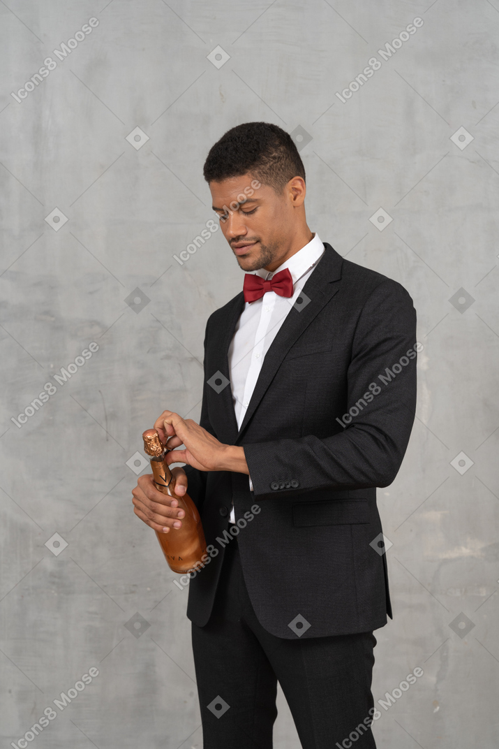 Junger mann im anzug, der eine champagnerflasche öffnet