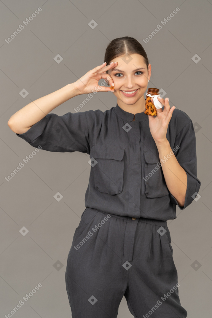 Vista frontal de una mujer joven en un mono tomando pastillas de un frasco