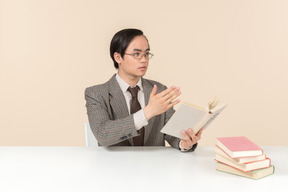 Un profesor asiático con traje a cuadros, corbata y un libro en la mano, trabajando con la clase.