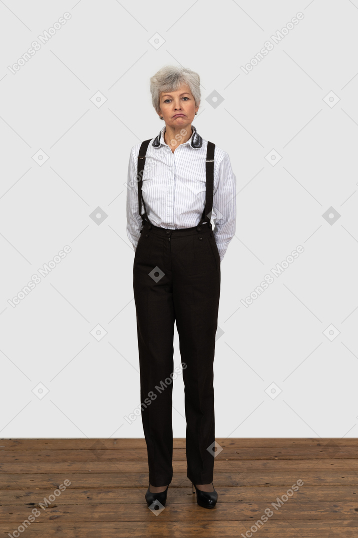 Front view of an old  displeased female in office clothes with her hands  behind back