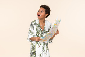 Mujer negra de pelo corto con un vestido blanco y verde, de pie con un mapa en las manos