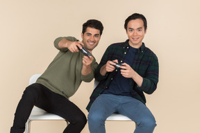 Interracial friends sitting in chairs and playing video games