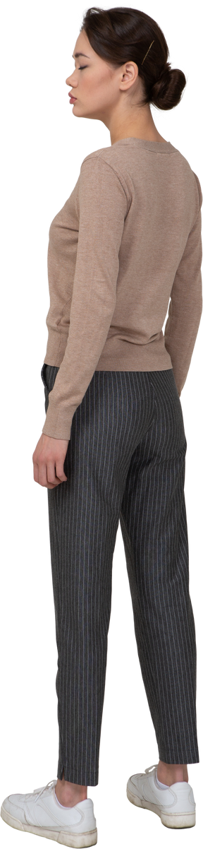 Vista posterior de tres cuartos de una joven de pie quieta en jersey y pantalones con los ojos cerrados