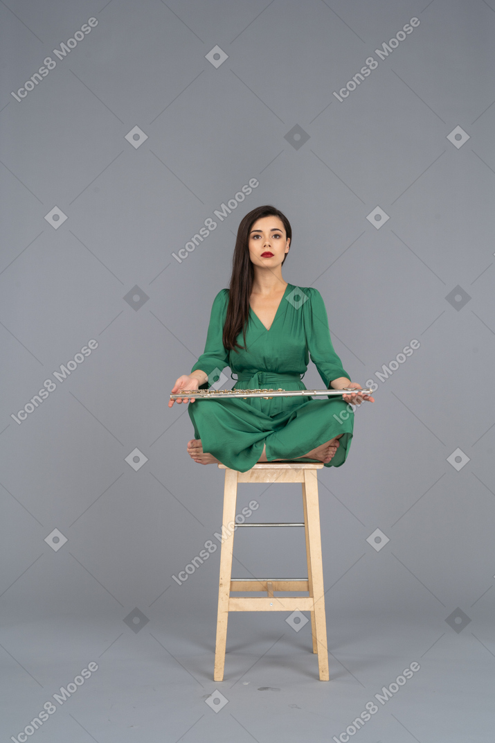 木製の椅子に座ってクラリネットを膝に抱えた若い女性の全身像
