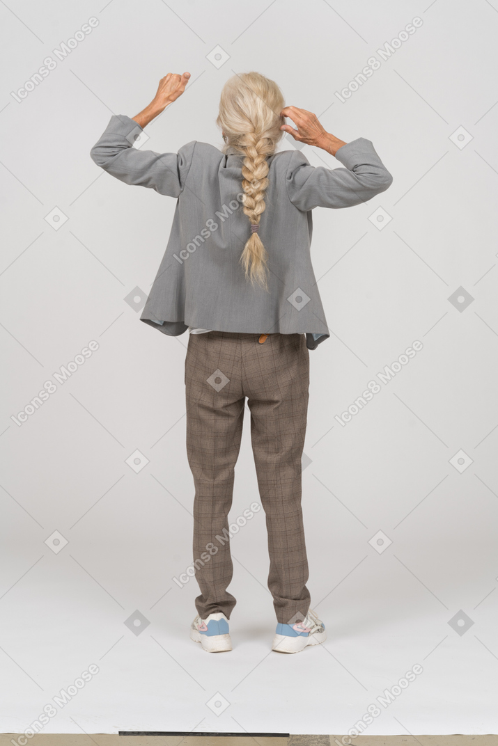 Вид сзади на старушку в костюме, стоящую с поднятыми руками