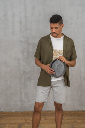 Man in casual clothes looking down while holding hat