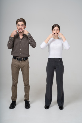 Vista frontal de um jovem casal com roupas de escritório esticando a boca